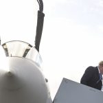 Boris Johnson walks down a staircase in front of an open fighter jet cockpit.