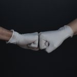 Two gloved hands fistbumping against a dark background.
